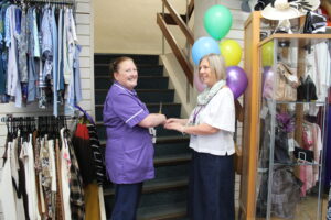 A nurse in purple uniform, and Community Shop Manager in a white shirt cut a ribbon to the entrance of a staircase. 