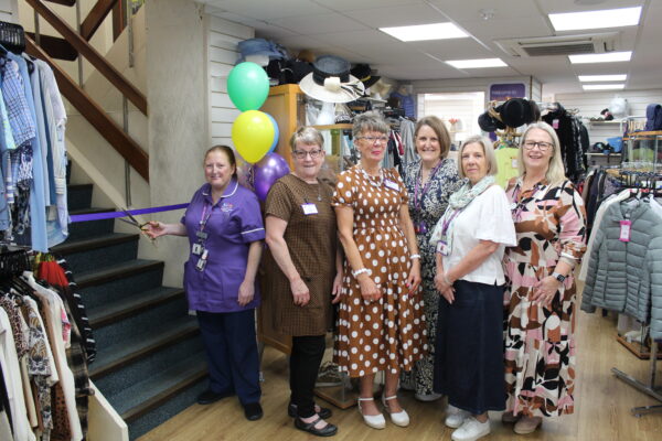 A group of women stand beside a lady in a purple nurses uniform as she cuts a ribbon in a doorway.