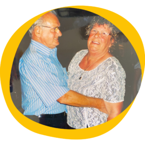 An older pictures shows a man in a blue shirt dancing with a lady in glasses. 