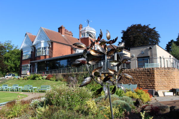 A sunny Hospice building, with a bronze garden decoration in the forefront.